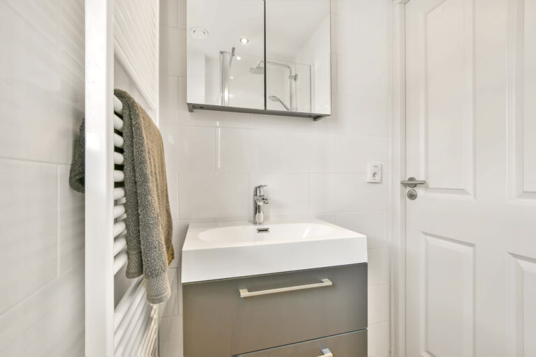 Bathroom with white tiles, ceramic sink under a mirrored wardrobe in a modern house